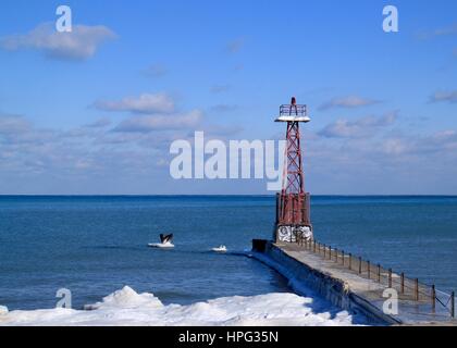 Lighthouse on Pier Jutting out into Lake Michigan on Frigid Winter Day in January with Frozen Lake Water Stock Photo