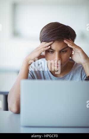 Tensed schoolboy looking at laptop in classroom at school Stock Photo