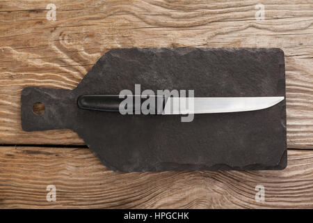 Knife on black slate plate against wooden background Stock Photo