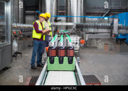 Two factory workers monitoring cold drink bottles on production line at drinks production plant Stock Photo
