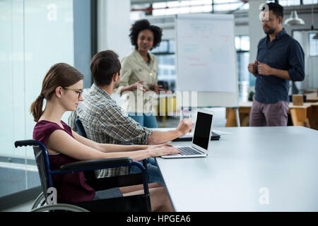 Disabled business executive in wheelchair working on laptop in meeting at office Stock Photo