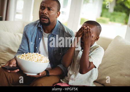 Son covering his eyes while watching television with father at home Stock Photo