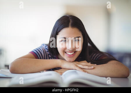 Portrait of happy schoolgirl leaning on bench in classroom at school Stock Photo