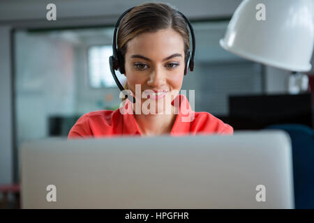 Smiling female executive working on her laptop while calling in office Stock Photo