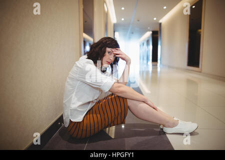 Portrait of sad female executive sitting in corridor in office Stock Photo