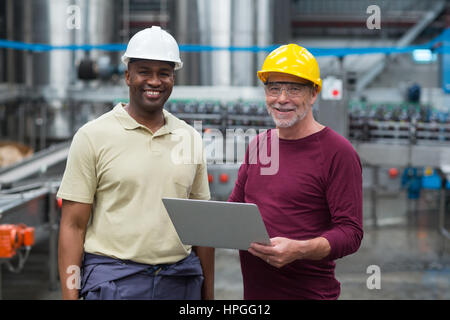 Portrait of two factory workers with laptop smiling in the drinks production plant Stock Photo