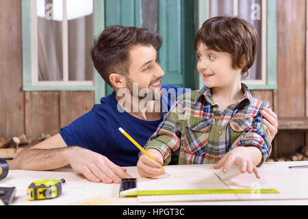 father helping son to take measures of wooden plank in workshop Stock Photo