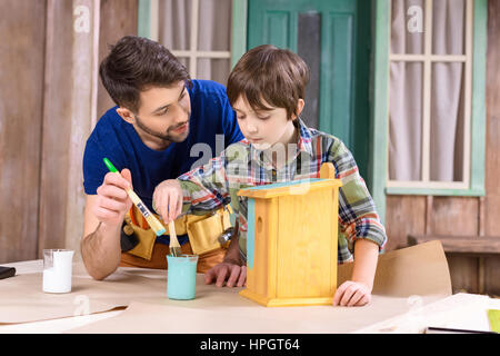 father and son painting wooden birdhouse together Stock Photo