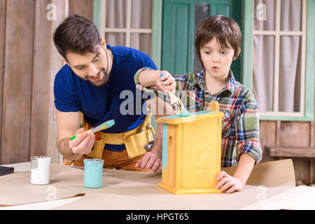 father and son with paintbrushes painting wooden birdhouse together Stock Photo