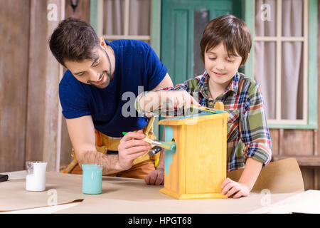 father and son painting wooden handmade birdhouse together Stock Photo