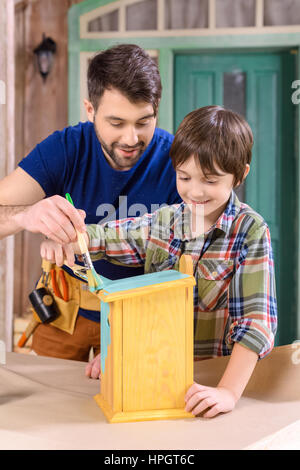 father and son painting wooden handmade birdhouse in workshop Stock Photo