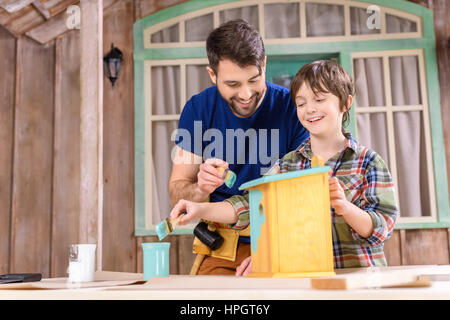 happy father and son painting wooden birdhouse on porch Stock Photo