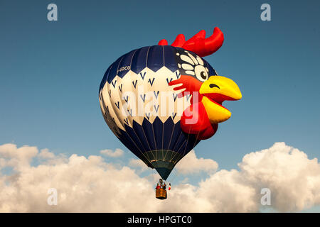 A hot air balloon shaped like a cockerel on a blue sky with low clouds Stock Photo