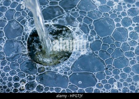 Water feature in a garden pond cascading water through a hole in the ice with bubbles forming underneath Stock Photo