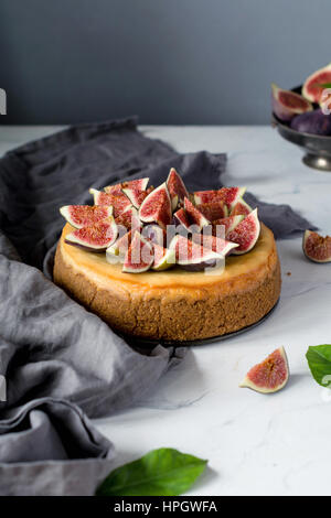 Whole cheesecake decorated with fresh figs on a marble table. Vertical view, copy space for text