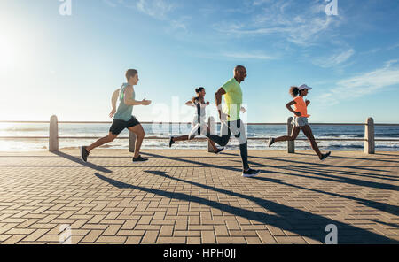 Full length shot of young people running along seaside. Group of runners working out on a road by the sea. Stock Photo