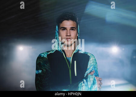 Portrait of urban runner standing on the street at night. Young man in sportswear standing under bridge.