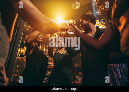 Low angle shot of group of friends enjoying drinks at bar together. Young people at nightclub toasting cocktails. Stock Photo