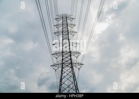 Silhouette of electricity post on blue sky background, low angle shot, high voltage electric pole, high voltage power supply on cloudy day. Stock Photo