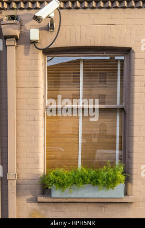 Close up on a window in a dark cream brick wall of a house protected with security cameras pointing to the left Stock Photo