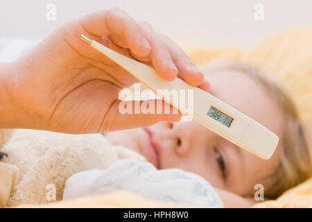 Krankes Maedchen liegt mit Fieberthermometer im Bett - sick girl with clinical thermometer in bed, Model released