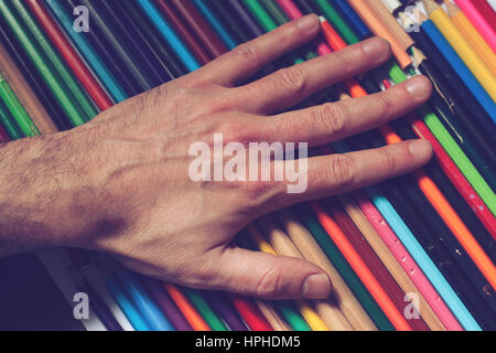 Horizontal top view close up of a male Caucasian hand touching  a set of many colored pencils Stock Photo