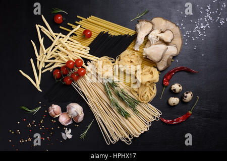 Mixed dried pasta selection with fresh ingredients: quail eggs, mushrooms, tomatoes, pepper, rosemary, garlic. Top view. Stock Photo