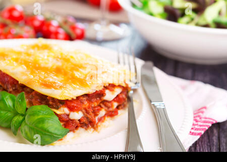 A portion of homemade lasagna on a plate, served with a salad on the side. Stock Photo