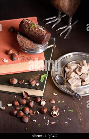 Chocolate truffle cake with cocoa powder, hazelnuts and mint on books, rustic wooden table. Top view. Stock Photo