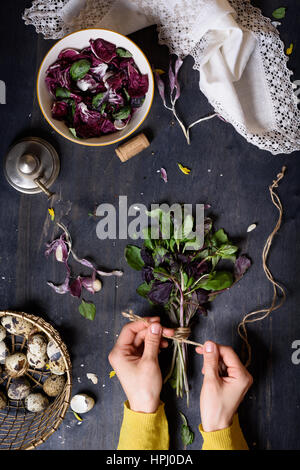 Herbs, gathered into a bunch and tied, over rustic table with salad and farm eggs. Overhead view. Healthy diet background. Stock Photo