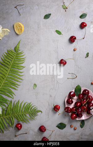 Fresh fruit, cherries and clafouti dessert on grey concrete background,decorated with fern and lemon. Copy space, view from above. Stock Photo