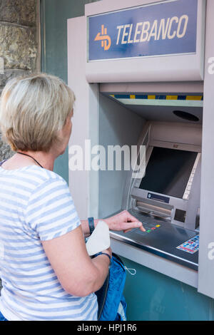 A woman using a telbanco or atm cash machine hole in the wall in Spain. Getting money when on holiday. Stock Photo