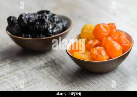 two plates with dried fruits on wooden background: dried mandarins and prunes. Stock Photo