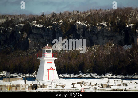 Snow covered lighthouse with background of a limestone cliff on the Bruce Peninsula. Ontario. Lions Head. Stock Photo