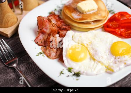 Tasty breakfast with fried eggs, pancakes, bacon and vegetables. Stock Photo