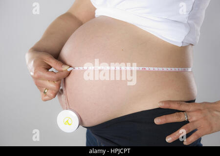 Model released , Schwangere Frau misst Bauchumfang mit Massband - pregnant woman measuring pregnant belly Stock Photo