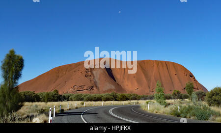 Ayers Rock contrasted by bright blue sky with the moon visible. Stock Photo