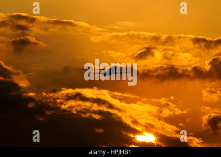 Silhouette of Fokker passenger regional jet taking off in sunset with orange-lit clouds in background Stock Photo