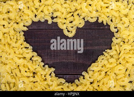 Raw macaroni - pasta Galetti.  In the middle of the empty space in the shape of a heart on a dark wooden background. Stock Photo
