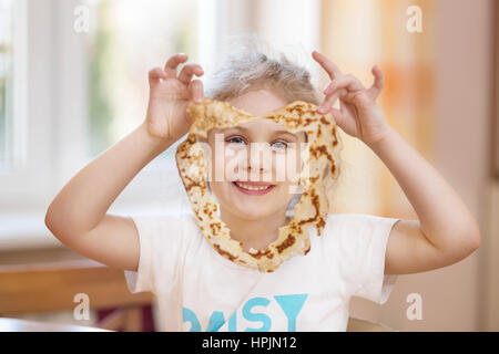 Cheerful girl with pancake in the kitchen at home Stock Photo