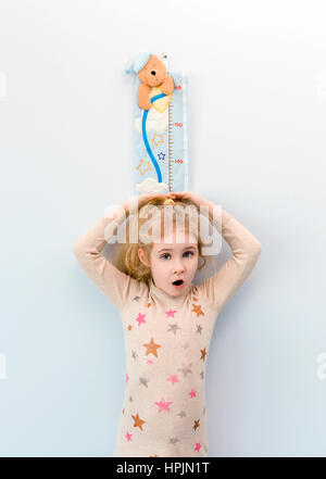 Little blonde girl measuring height against wall in room Stock Photo