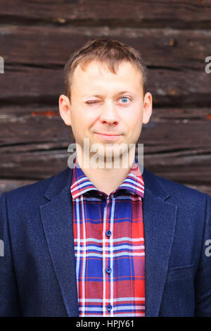 Blinking man in blue jacket and checkered shirt on wood background Stock Photo