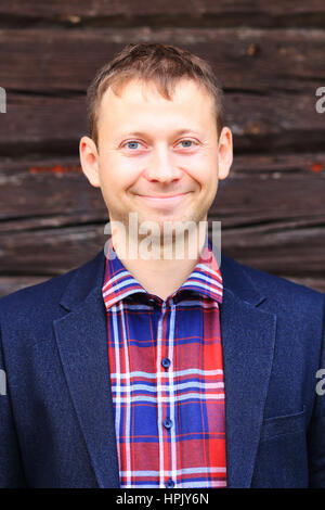 Smiling man in blue jacket and checkered shirt on wood background Stock Photo