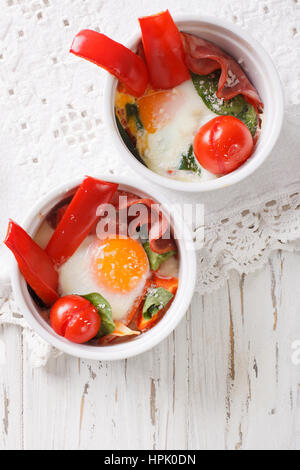 Baked egg with spinach, peppers, tomatoes and cheese in a cup close-up on the table. vertical view from above Stock Photo