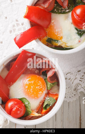Tasty breakfast: fried eggs with vegetables and cheese in a cup close-up on the table. vertical view from above Stock Photo