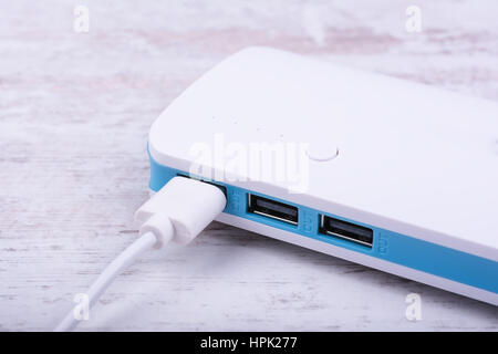 Portable power bank for charging mobile devices on white wooden background. Stock Photo