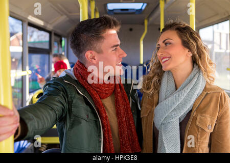 Young couple posing on a bus for the camera. They are standing and there are people sitting on the bus in the background. Stock Photo