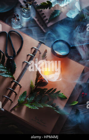 Botanical still life with a herbarium of glowing flower, old books, magical smoke and a magnifying glass Stock Photo