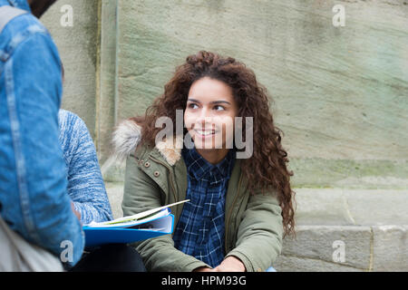 A happy female student smiles as she stands amongst her friends outdoors. They are taking a break from university in the city centre. Stock Photo