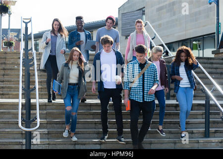 A group of young teenage students smile as they walk through the city on a break from university. They are carrying their books and digital tablets. Stock Photo